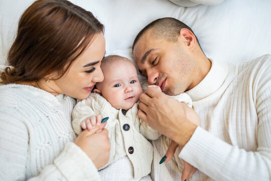 Happy family with one baby spending time at home. Parents playing with their baby on bed.