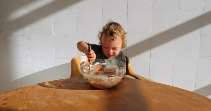 Toddler is earnestly engaged in helping with important task of making chocolate pancakes. He appears fully concentrated, although in reality, he's playfully dawdling with sticky batter