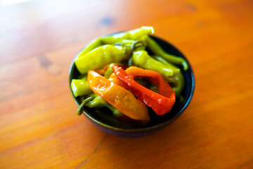 Different colored Pepperoni in a black bowl on an orange table