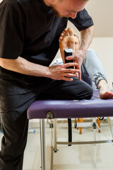 Male physiotherapist doctor massages the feet of a relaxed man sitting on a stretcher. He uses kinesio tape. Taping the foot - obrazy, fototapety, plakaty