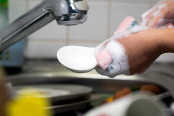A hand with a dishwashing sponge washing the dishes and ladle. 