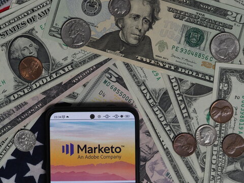 In this photo illustration, a Marketo, Inc. logo seen displayed on a smartphone with United States Dollar notes and coins in the background.