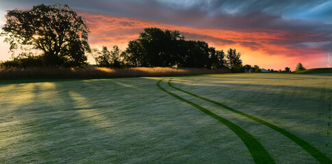 Golf cart tracks on a golf course during a dramatic sunrise