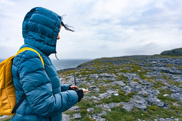 Woman with hood sheltering from the wind on a pristine, natural coastline in Ireland while looking...