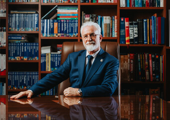 Caucasian university rector in 60s or 70s, poses confidently in a book-filled library. Mature...