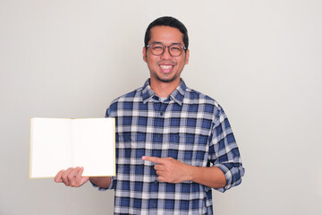 Adult Asian man smiling at the camera and pointing to blank book pages that he show
