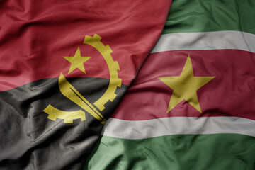 big waving national colorful flag of suriname and national flag of angola .