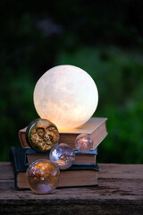 decorative moon lamp, moon amulet, crystal balls, books on table outdoor, dark natural background....