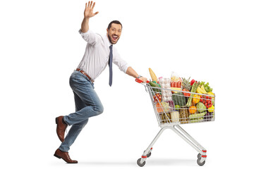 Cheerful man running with food in a shopping cart and waving at camera