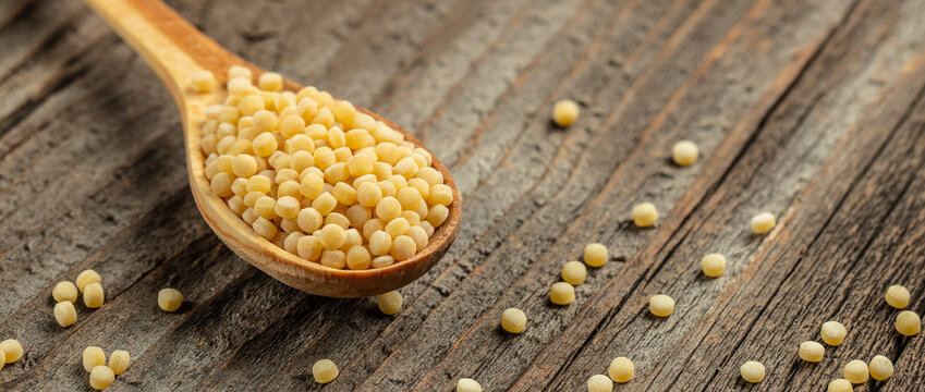 fregola pasta on a wooden spoon on a wooden background. Long banner format. top view. copy space for text