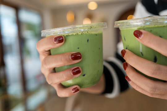 Close up image of a woman holding two glasses of iced matcha green tea in a minimal cafe