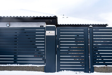 A modern gate with a letterbox and a wireless card reader, mounted in an anthracite panel fence,...