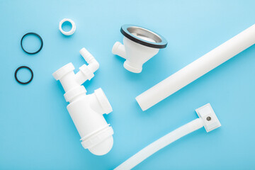 White new plastic parts for sink drain siphon assembling. Light blue table background. Pastel color. Closeup. Top down view.