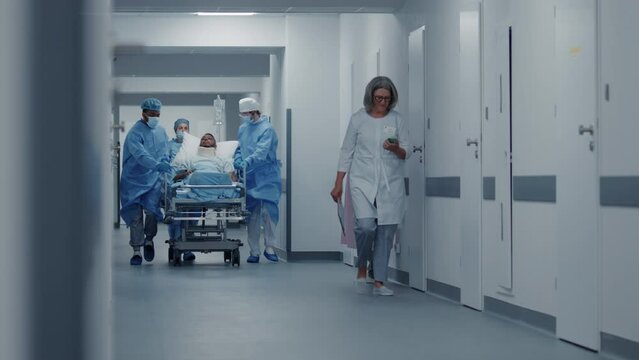 Doctors, nurses and paramedics push stretcher with patient and support him. African American man with neck brace lies on gurney. Multi ethnic medical staff work in emergency department. Slow motion.