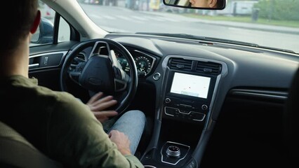 Male driver driving car, inside view. Rear view of man driving car in city street, looking around at road traffic and turning steering wheel. Safety ride