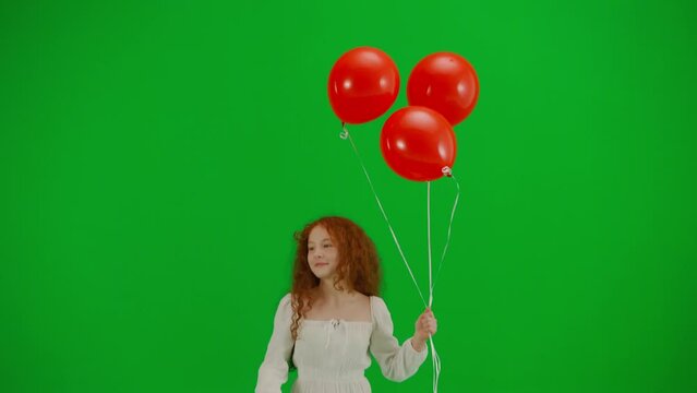 Little girl in white dress with red balloons on chroma key green screen isolated background running looking at the camera, positive face.