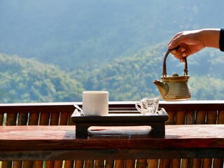 A hand pouring tea from glass teapot on wooden serving tray, hands pouring tea from teapot, Cropped...