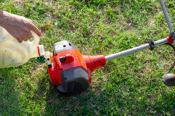 gardener fills a lawn mower with a mixture of gasoline and oil. Maintenance of garden equipment