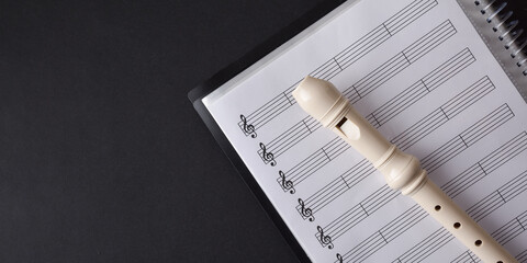 Plastic recorder on sheet music folder on a black table