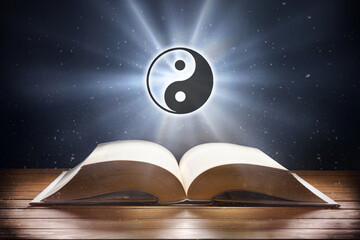 Open book on wooden table and taoist symbol front view
