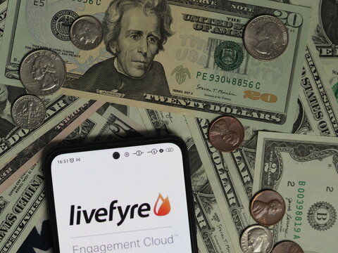 In this photo illustration, a Livefyre logo seen displayed on a smartphone with United States Dollar notes and coins in the background. Livefyre  subordinary of Adobe Inc.  corporation