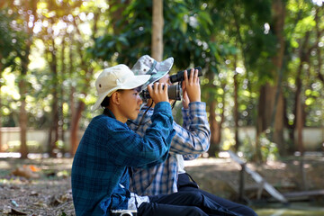 Asian boys use binoculars to look at birds in a community forest own. The concept of learning from learning sources outside the school. Focus on the first child.