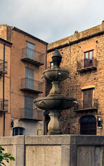 Detailed view ancient stone fountain on the city square in the downtown of Castelbuono village, Sicily, Italy. Old houses in the background. Travel and tourism concept