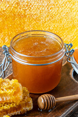 A glass jar of thick golden honey with wooden spoon and honeycombs. Concept of beekeeping, apiculture, apiary. Sweet honey product, healthy food