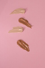 Various shades of foundation on a pink background, Makeup foundation cream strokes of different...