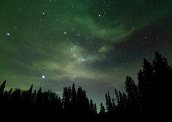 A night sky image of a star filled sky with thin cloud lit up by a distant green Aurora. The...
