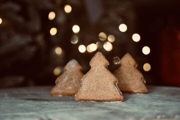 Christmas tree biscuits on wooden table with out of focus lights in the background.