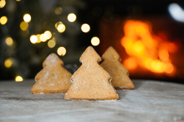 Close-up of biscuits in the shape of a Christmas tree with blurred lights and a lit fireplace in...