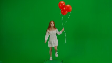 Little girl in white dress with red balloons on chroma key green screen isolated background running looking at the camera, positive face.