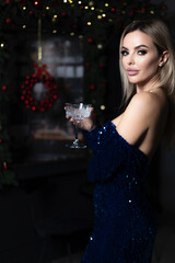 beautiful girl with a glass of champagne celebrates the holiday in a shiny long blue dress