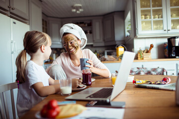 Daughter having breakfast with mother and using laptop
