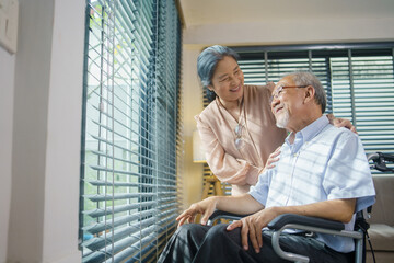 Asian grandmother takes care of her patient husband sitting on wheelchair at home. Senior couple...