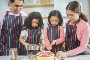 Diverse family baking bakery together in the kitchen on weekend. Parent taking care and teaching daughters to cook. Love and bonding concept