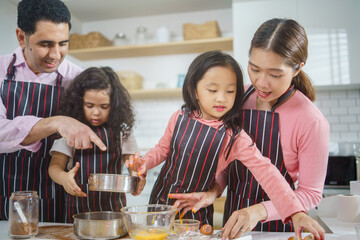 Diverse family baking bakery together in the kitchen on weekend. Parent taking care and teaching daughters to cook. Love and bonding concept