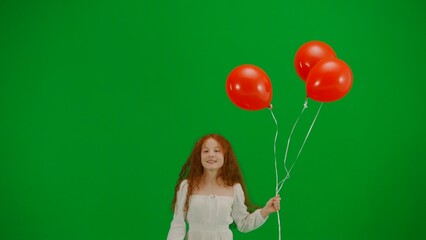 Little girl in white dress with red balloons on chroma key green screen isolated background running looking at the camera, positive face.