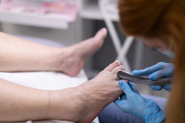 The cosmetologist removes keratinized skin from the feet with pliers.