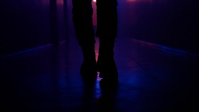 Portrait of female in the dark hallway neon light. Close up shot from the floor girl alone walking down the dark empty corridor.