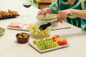 Hands of party guest putting salad in her plate