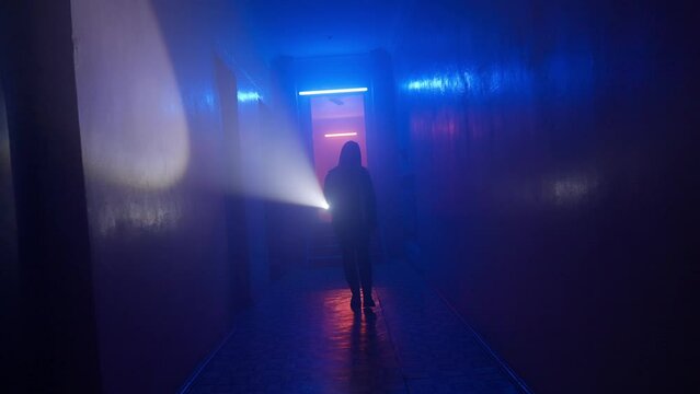 Portrait of female in the dark hallway with neon light. Woman with flashlight facing the camera walking down alone in the corridor.