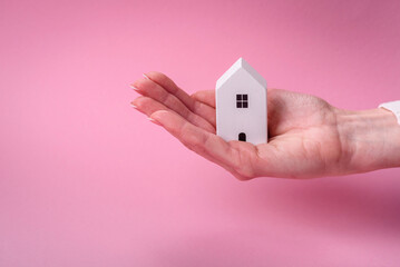 Female hands, a small wooden house and keys as an idea for investing in your own home and achieving...