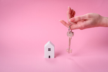 Female hands, a small wooden house and keys as an idea for investing in your own home and achieving...