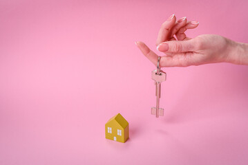 Female hands, a small wooden house and keys as an idea for investing in your own home and achieving the goal of buying real estate
