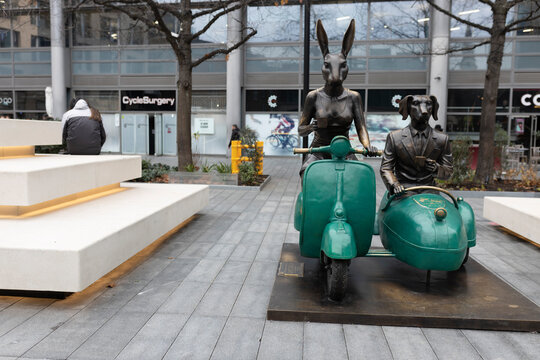 Spitalfields market, London UK - 19 December 2023, Rabbitwoman and Dogman, Vespas, and coffee. Gillie Marc Tandem Lovers sculpture of Rabbitwoman and Dogman, illustrating scene in dark tones