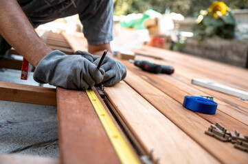 Worker with protective gloves marking a spot on wooden plank while placing it on a foundation for outside patio - obrazy, fototapety, plakaty