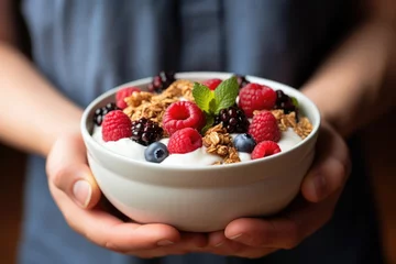 Fotobehang A person holding a bowl of yogurt and berries. © tilialucida