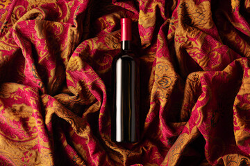 Bottle of red wine on a retro tapestry with dark red and golden floral ornament.